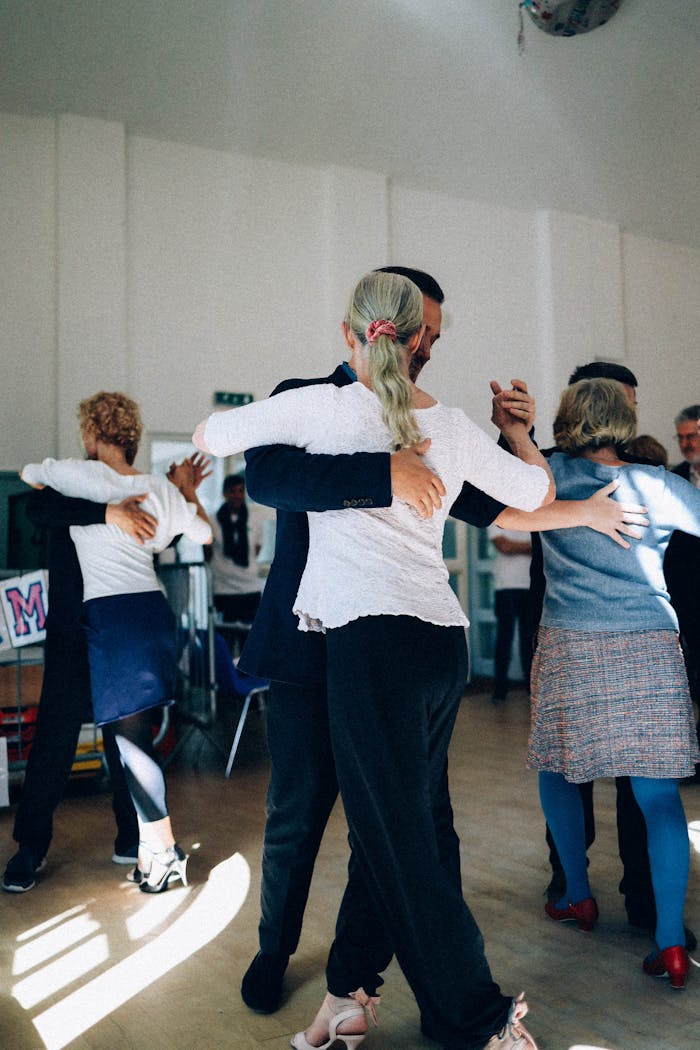 hero-img A group of adults practicing ballroom dancing in a sunlit indoor studio, capturing elegance and grace.